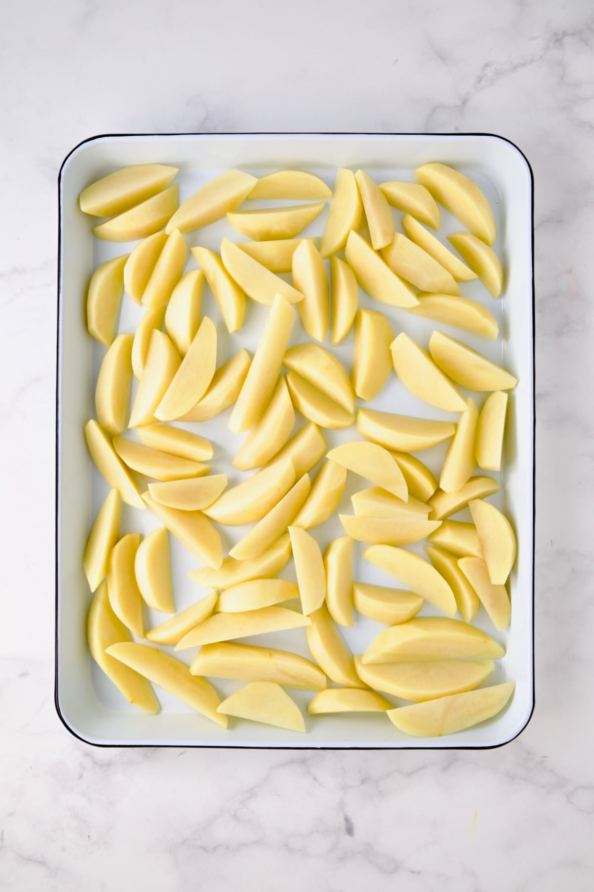 Peeled wedges of Yukon Gold potatoes on white enamel rimmed sheet pan.