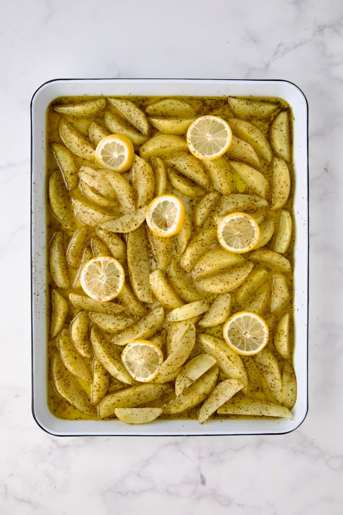 Partially cooked peeled wedges of Yukon Gold potatoes on white enamel rimmed sheet pan.
