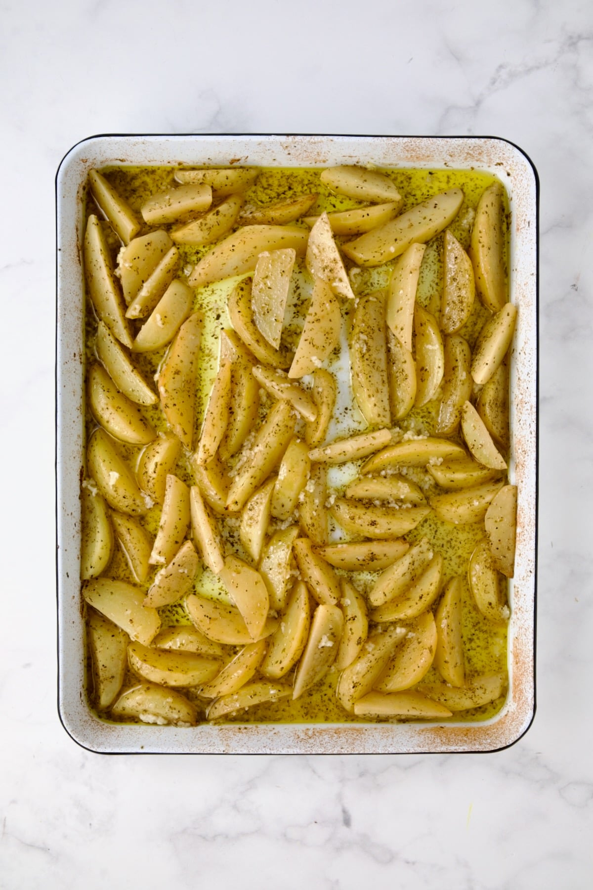 Partially cooked peeled wedges of Yukon Gold potatoes on white enamel rimmed sheet pan with garlic added.