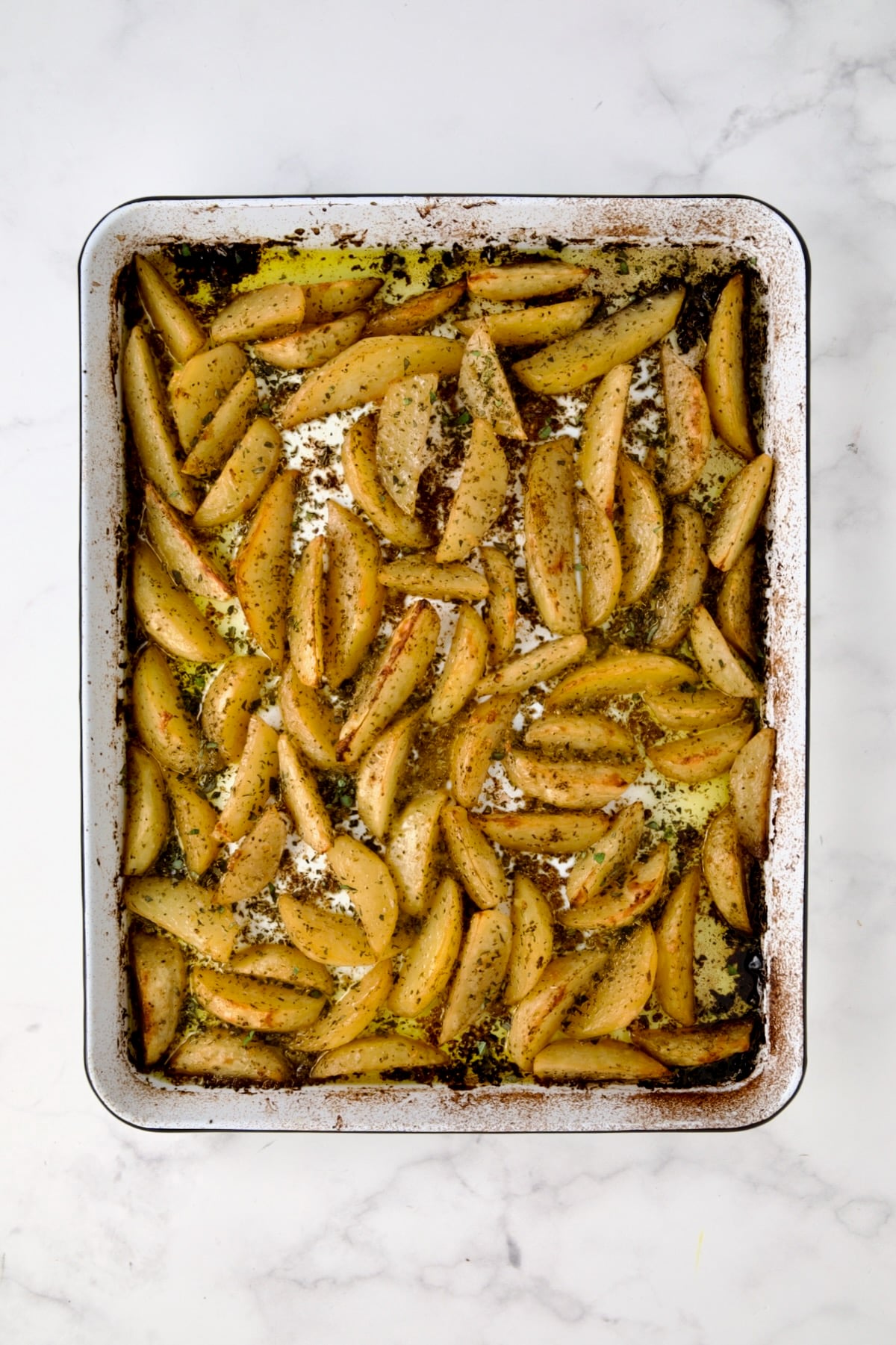 Cooked peeled wedges of Yukon Gold potatoes on white enamel rimmed sheet pan.